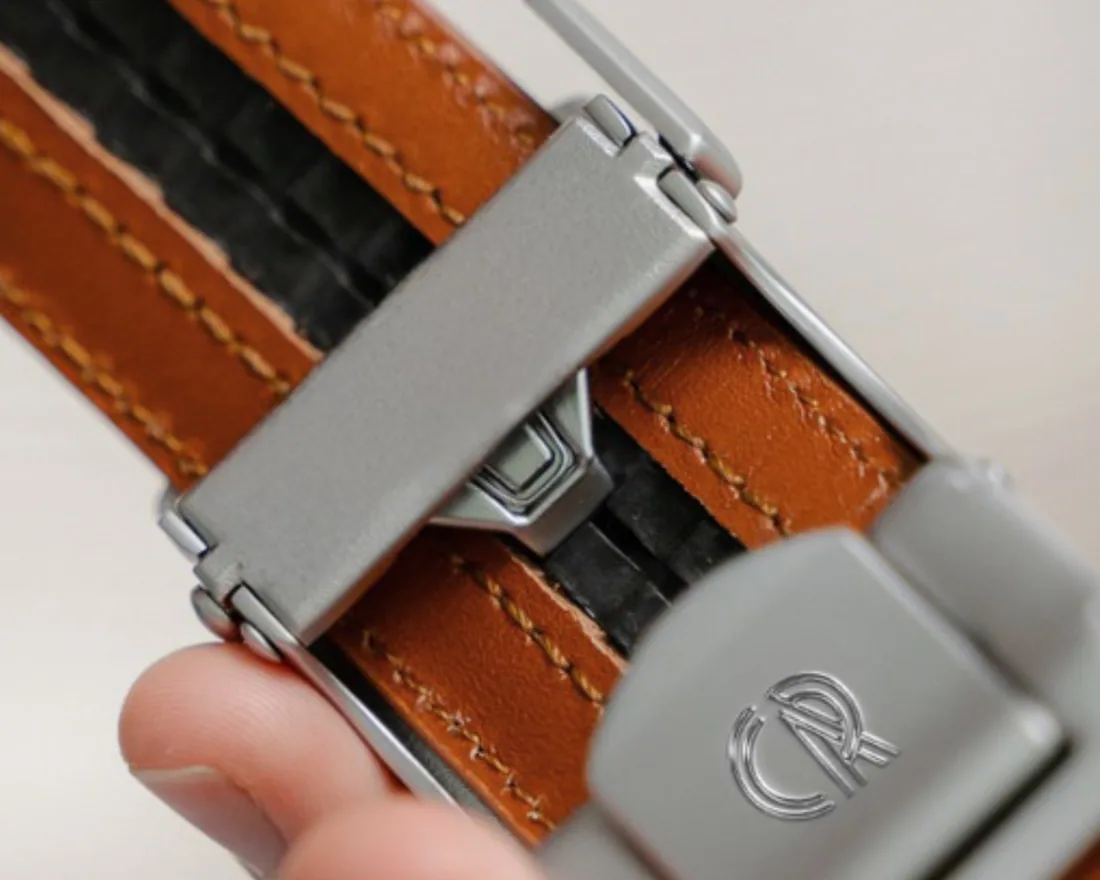 A CHAOREN ratchet buckle held against a brown leather strap